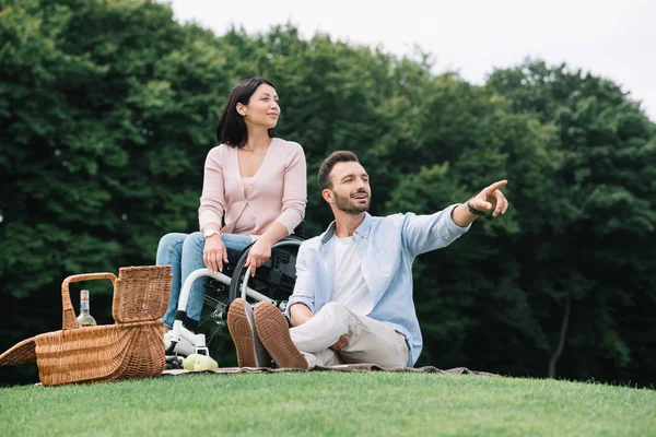 Hombre guapo señalando con el dedo mientras descansa en el parque con la novia discapacitada - foto de stock