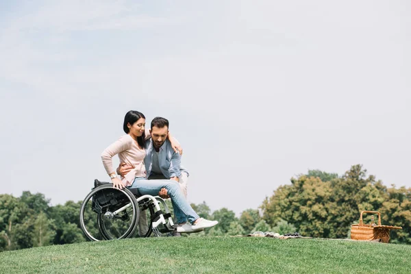 Handsome young man taking young disabled girlfriend out of wheelchair — Stock Photo