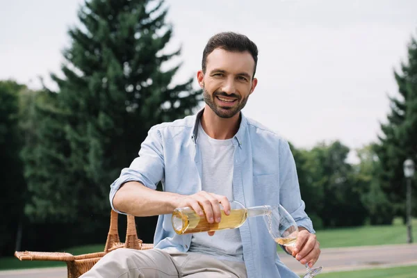 Fröhlicher Mann lächelt in die Kamera, während er Weißwein ins Glas gießt — Stockfoto