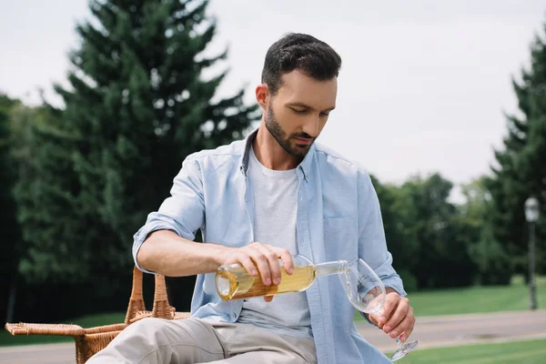 Homem bonito derramando vinho branco em vidro no parque — Fotografia de Stock