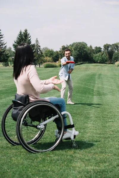 Веселий молодий чоловік кидає літаючий диск інвалідній дівчині в парку — стокове фото