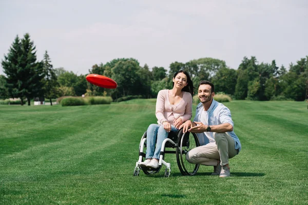 Smiling man throwing flying disc near young disabled girlfriend in park — Stock Photo