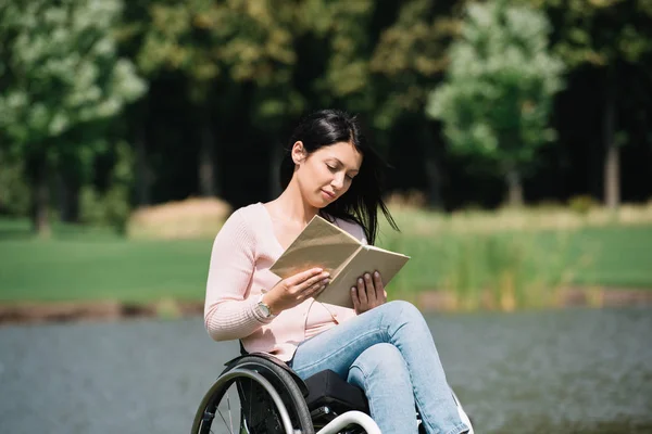 Hermosa mujer discapacitada sonriendo mientras lee libro en el parque - foto de stock