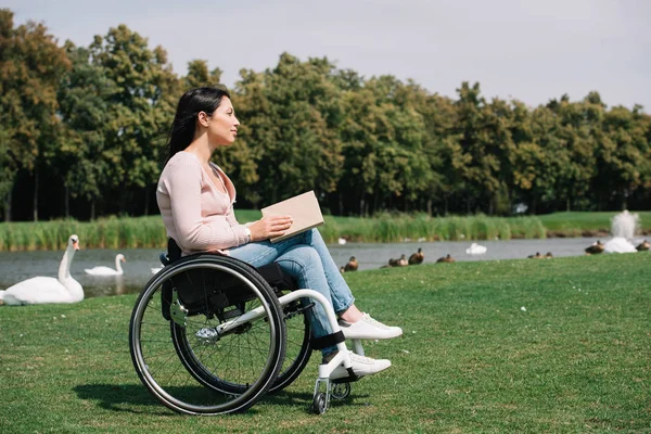 Verträumte behinderte Frau hält Buch in der Nähe von Teich mit Vögeln — Stockfoto