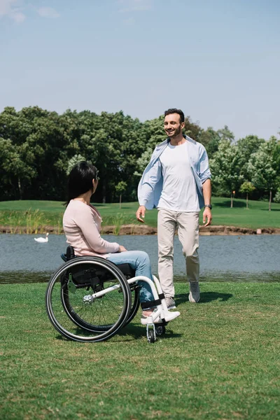 Allegro giovane con ragazza disabile che riposa vicino al lago nel parco — Foto stock