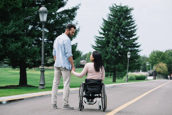 Back view of young disabled woman holding hands with handsome boyfriend while walking in park together — Stock Photo