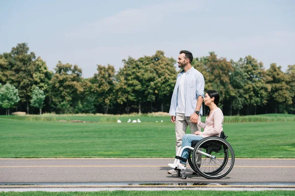 Bonito jovem homem de mãos dadas com deficiência namorada enquanto caminhando no parque juntos — Stock Photo