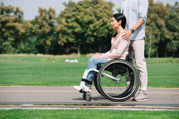 Обрезанный вид молодого человека, прогуливающегося в парке с девушкой-инвалидом — стоковое фото