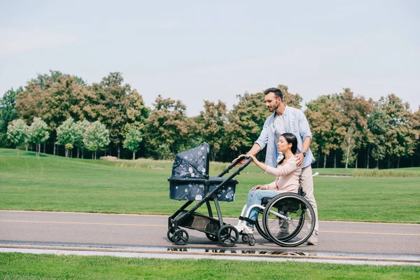 Homem bonito e mulher deficiente andando com carrinho de bebê no parque juntos — Fotografia de Stock