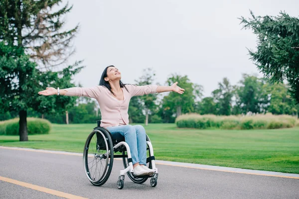 Femme handicapée heureuse en fauteuil roulant gestuelle tout en regardant le ciel clair — Photo de stock