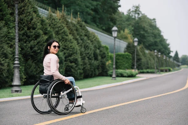 Young disabled woman in sunglasses looking at camera while walking in park — Stock Photo