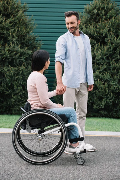 Happy man holding hands with disabled girlfriend while walking in park together — Stock Photo