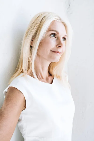 Smiling blonde mature woman looking away near white wall — Stock Photo