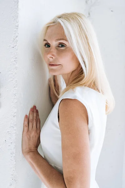 Dreamy blonde mature woman near white wall — Stock Photo