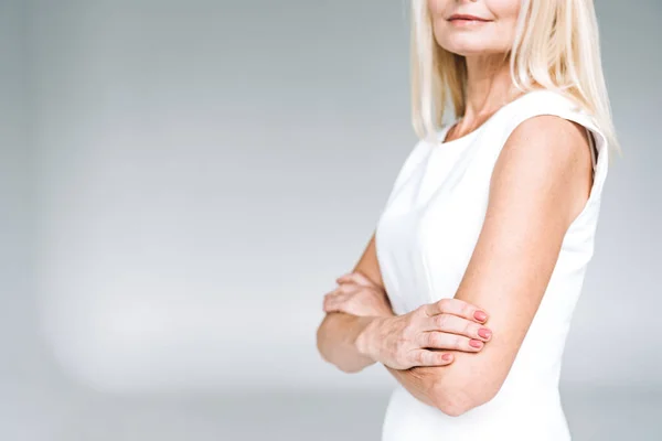 Partial view of blonde mature woman with crossed arms isolated on grey — Stock Photo