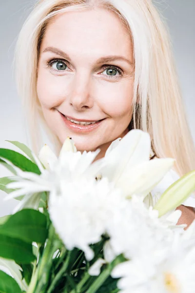 Porträt einer glücklichen blonden reifen Frau mit weißen Blüten, isoliert auf grau — Stock Photo