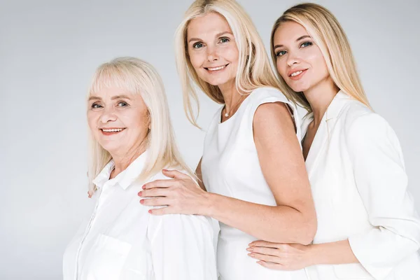 Vista lateral de mujeres rubias de tres generaciones aisladas en gris - foto de stock