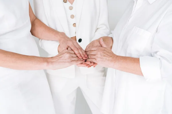 Обрезанный вид трех поколений женщин в белой одежде, держащихся за руки изолированы на сером — стоковое фото