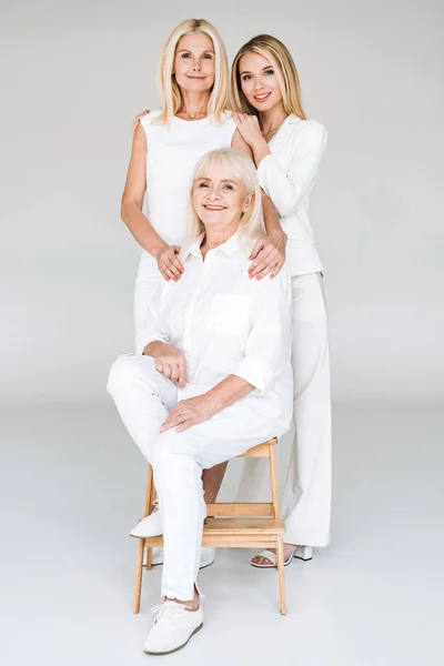 Блондинка мати і дочка стоять біля бабусі на дерев'яному стільці на сірому фоні — стокове фото