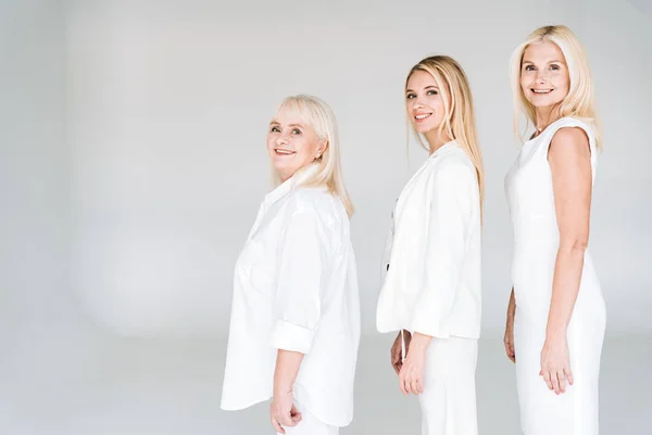 Seitenansicht der drei Generation blonder Frauen, die isoliert auf grau in die Kamera schauen — Stockfoto