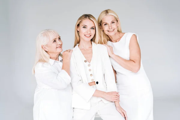 Mujeres rubias de tres generaciones sonriendo aisladas en gris - foto de stock