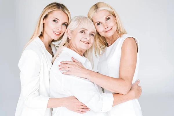 Три покоління блондинки обіймаються ізольовано на сірому — стокове фото