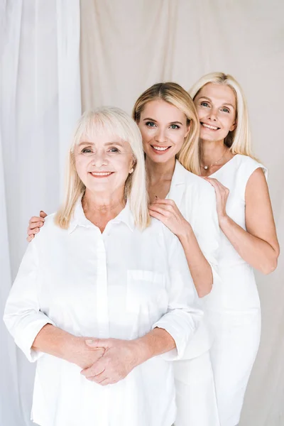 Elegantes mujeres rubias hermosas de tres generaciones en trajes blancos totales - foto de stock