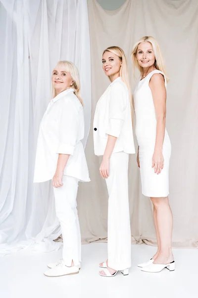 Vista lateral de mulheres loiras de três gerações felizes elegantes em roupas brancas totais — Fotografia de Stock