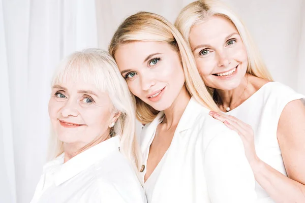 Sonriendo elegantes mujeres rubias de tres generaciones en trajes blancos totales - foto de stock