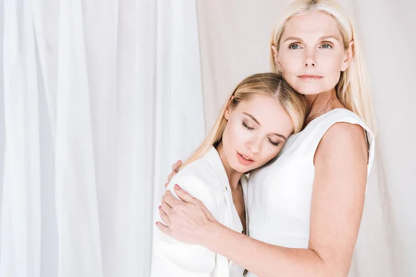 Hermosa elegante rubia madre e hija abrazando sobre fondo blanco - foto de stock