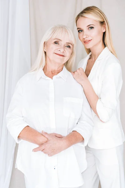 Elegante abuela rubia y nieta en trajes blancos totales - foto de stock