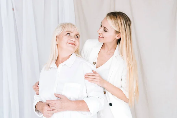 Elegant blonde grandmother and granddaughter in total white outfits looking at each other — Stock Photo