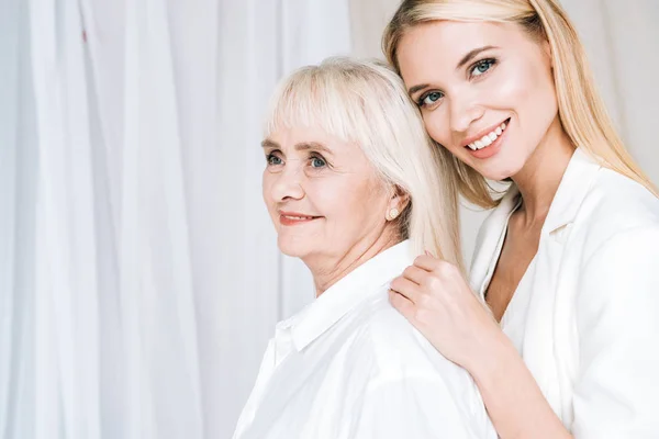 Элегантная блондинка-внучка обнимает улыбающуюся бабушку — стоковое фото