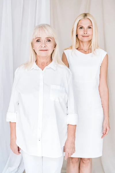Elegant blonde mature daughter and senior mother in total white outfits — Stock Photo