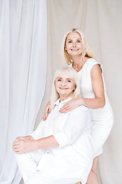 Happy blonde mature daughter and senior mother in total white outfits — Stock Photo