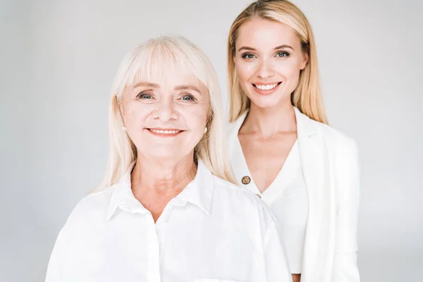 Smiling blonde grandmother and granddaughter together in total white outfits isolated on grey — Stock Photo