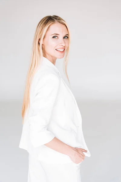 Усміхнена красива блондинка в загальному білому вбранні ізольована на сірому — стокове фото