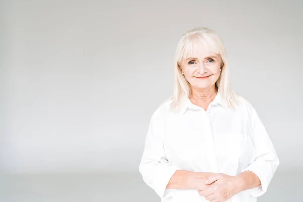 Happy blonde senior woman in white clothes isolated on grey — Stock Photo