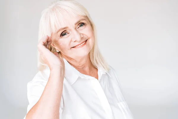 Glückliche blonde Seniorin blickt vereinzelt in die Kamera auf grau — Stockfoto
