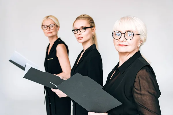 Mujeres de negocios de moda de tres generaciones en gafas con carpetas aisladas en gris - foto de stock