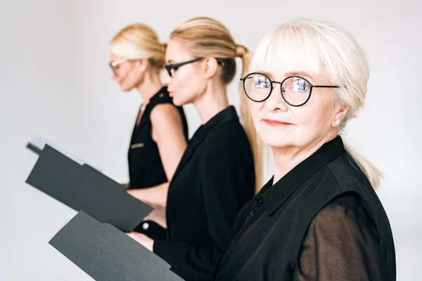 Mulheres de negócios de três gerações em óculos com pastas isoladas em cinza — Fotografia de Stock