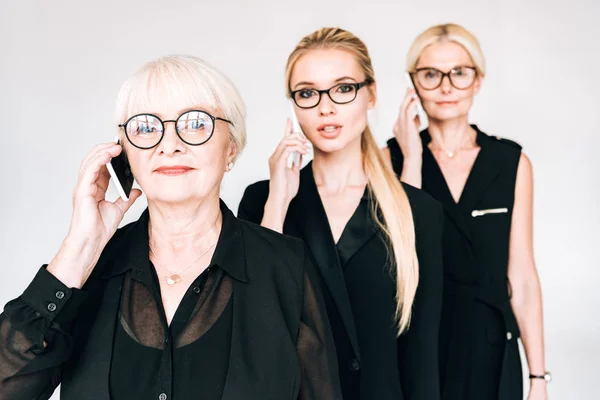 Mulheres de negócios de três gerações na moda falando em smartphones isolados em cinza — Fotografia de Stock