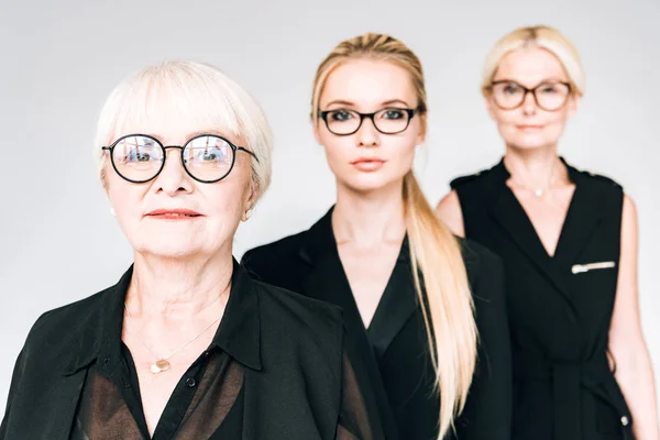 Mujeres de negocios rubias de moda de tres generaciones en gafas aisladas en gris - foto de stock