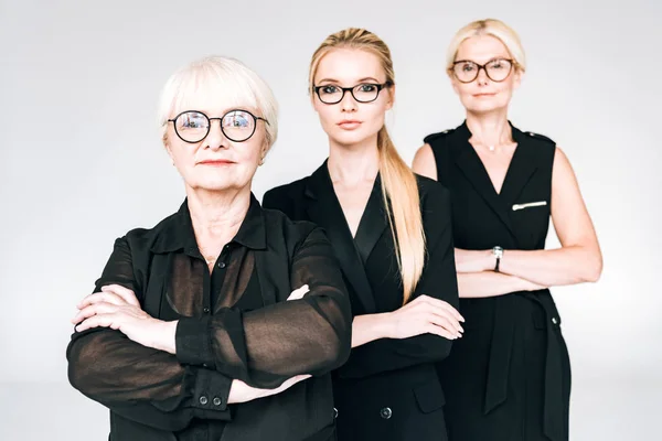 Fashionable three-generation blonde businesswomen in glasses with crossed arms isolated on grey — Stock Photo