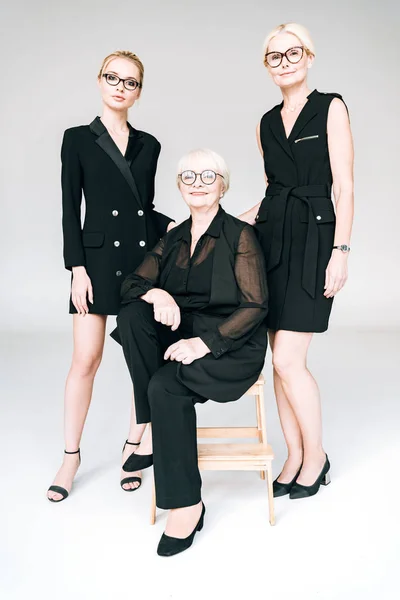 Vue pleine longueur des femmes d'affaires blondes à la mode de trois générations dans des lunettes avec les bras croisés isolés sur gris — Photo de stock