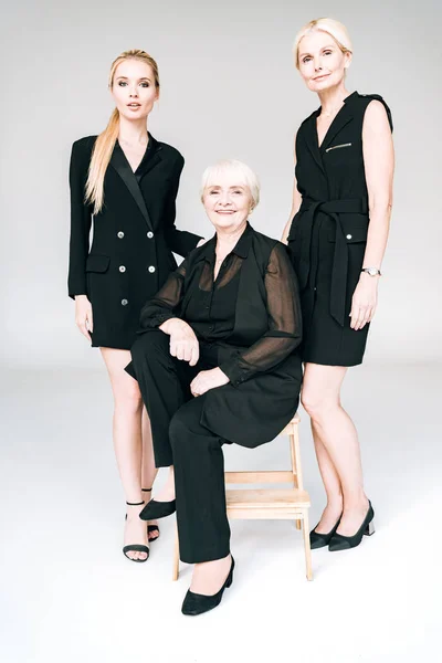 Full length view of elegant three-generation blonde women in total black outfits isolated on grey — Stock Photo