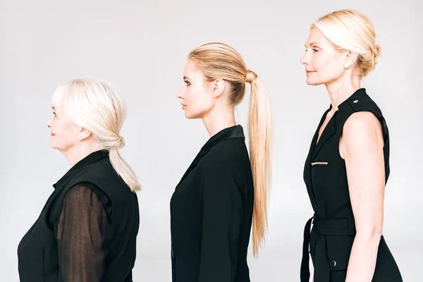 Side view of elegant three-generation blonde women in total black outfits isolated on grey — Stock Photo