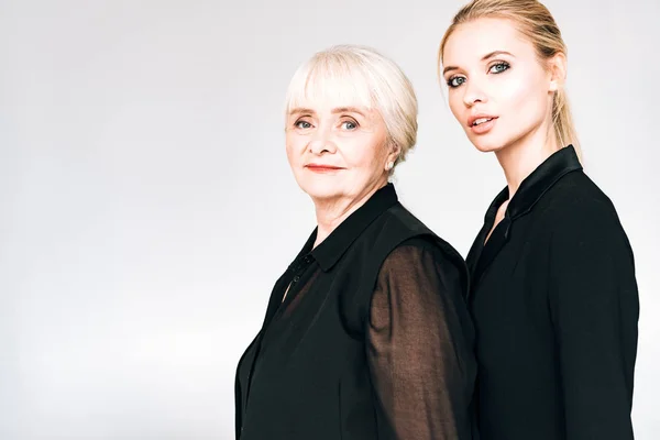 Elegante rubia nieta y abuela en total negro trajes aislado en gris - foto de stock