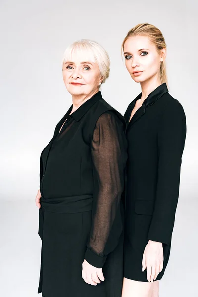 Elegant blonde granddaughter and grandmother in total black outfits isolated on grey — Stock Photo