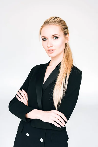 Mujer elegante en traje negro con brazos cruzados aislados en gris - foto de stock